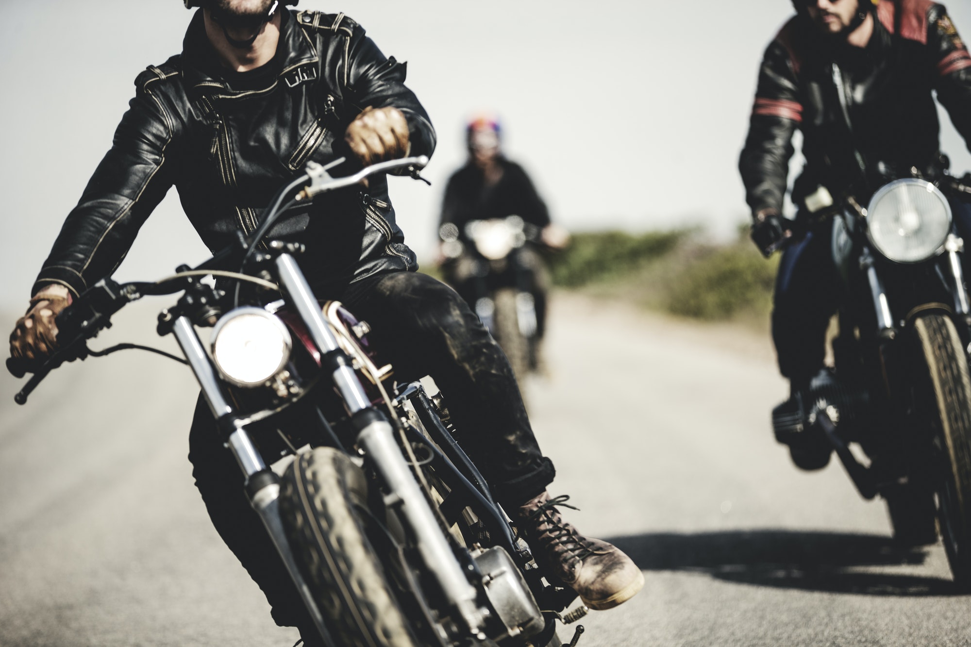 three-men-wearing-leather-jackets-riding-cafe-racer-motorcycles-along-rural-road-.jpg