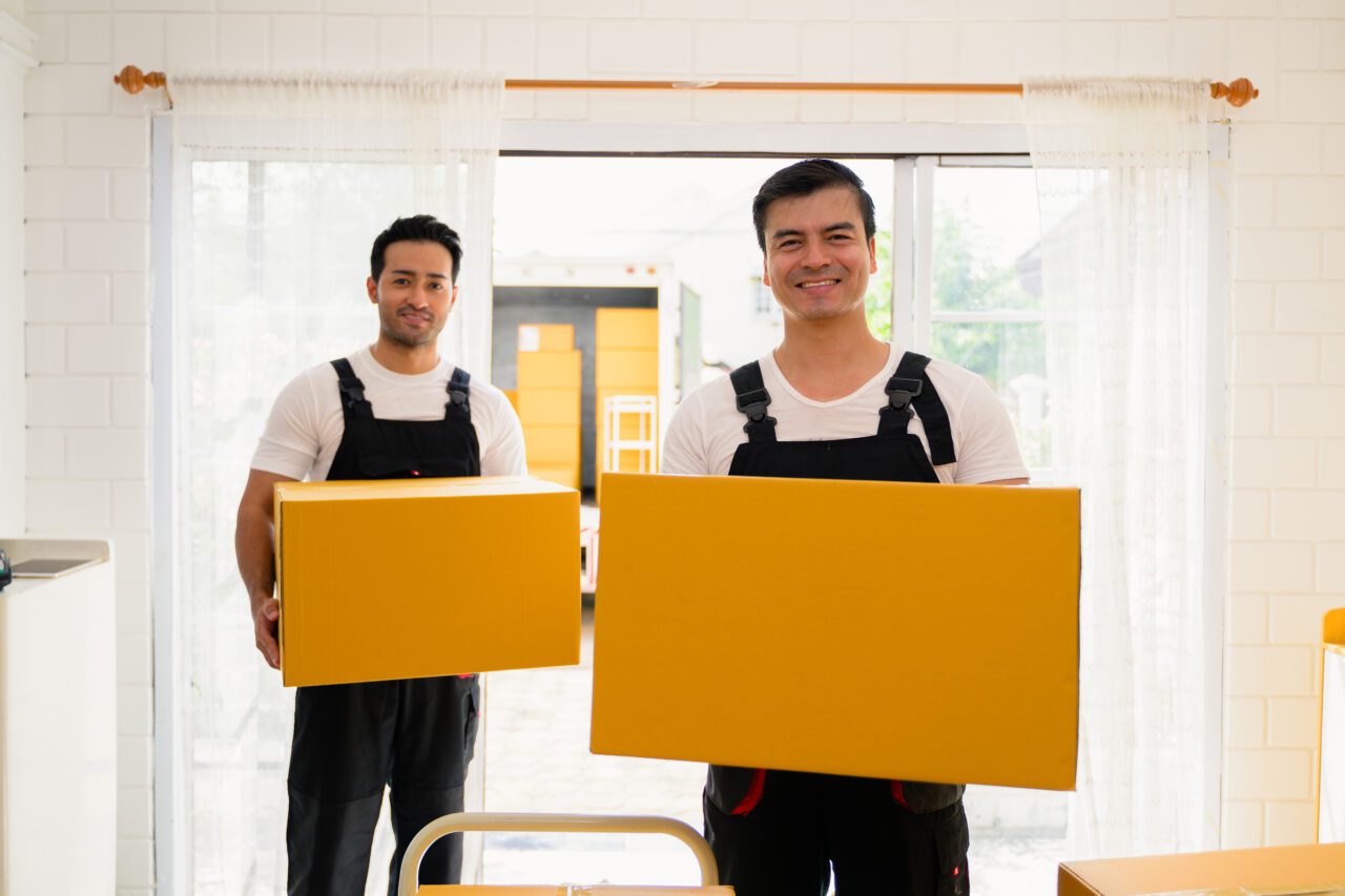 happy-two-delivery-men-holding-parcel-boxes-to-customer-delivery-men-checking-order-of-moving-e1696172084131.jpg